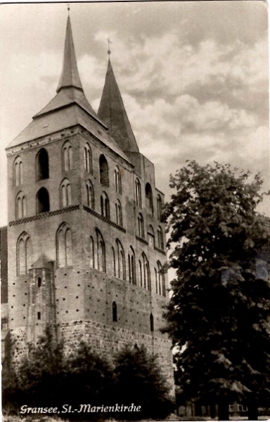 Historisches Gebäude mit zwei spitzen Türmen und Bäumen im Vordergrund.