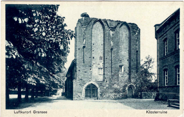 Ruine einer historischen Kirche mit hohen Mauern und Bäumen im Vordergrund.