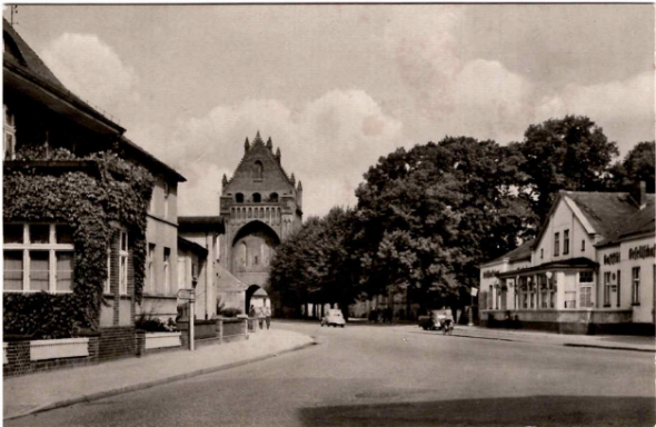 Schwarze und weiße Ansicht einer Straße mit historischer Stadtmauer und Bäumen.