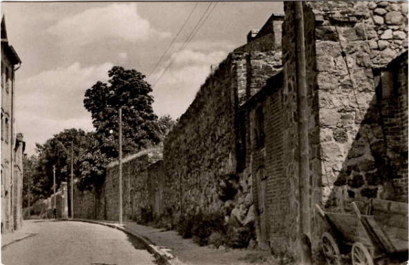 Schmale, gepflasterte Straße neben einer alten Steinmauer unter bewölktem Himmel.