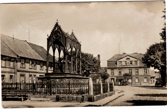 Historisches Stadtszenario mit einem Brunnen und alten Gebäuden im Hintergrund.