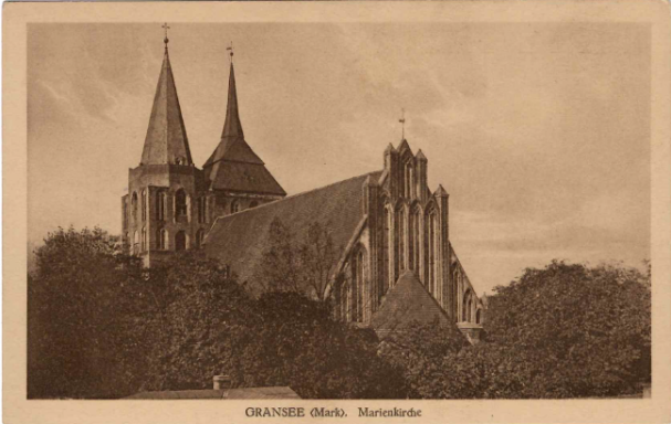 Backsteinkirche in Granseemit zwei markanten Türmen und umgebenden Bäumen.